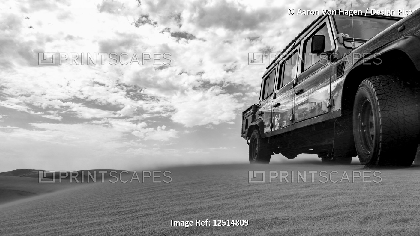 Black and white image of a recreational vehicle riding over the sand dunes, ...