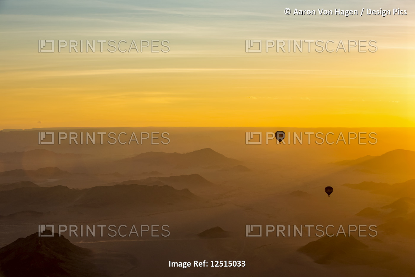 Silhouette of hot air balloons in the golden sky over the sand dunes at sunrise ...