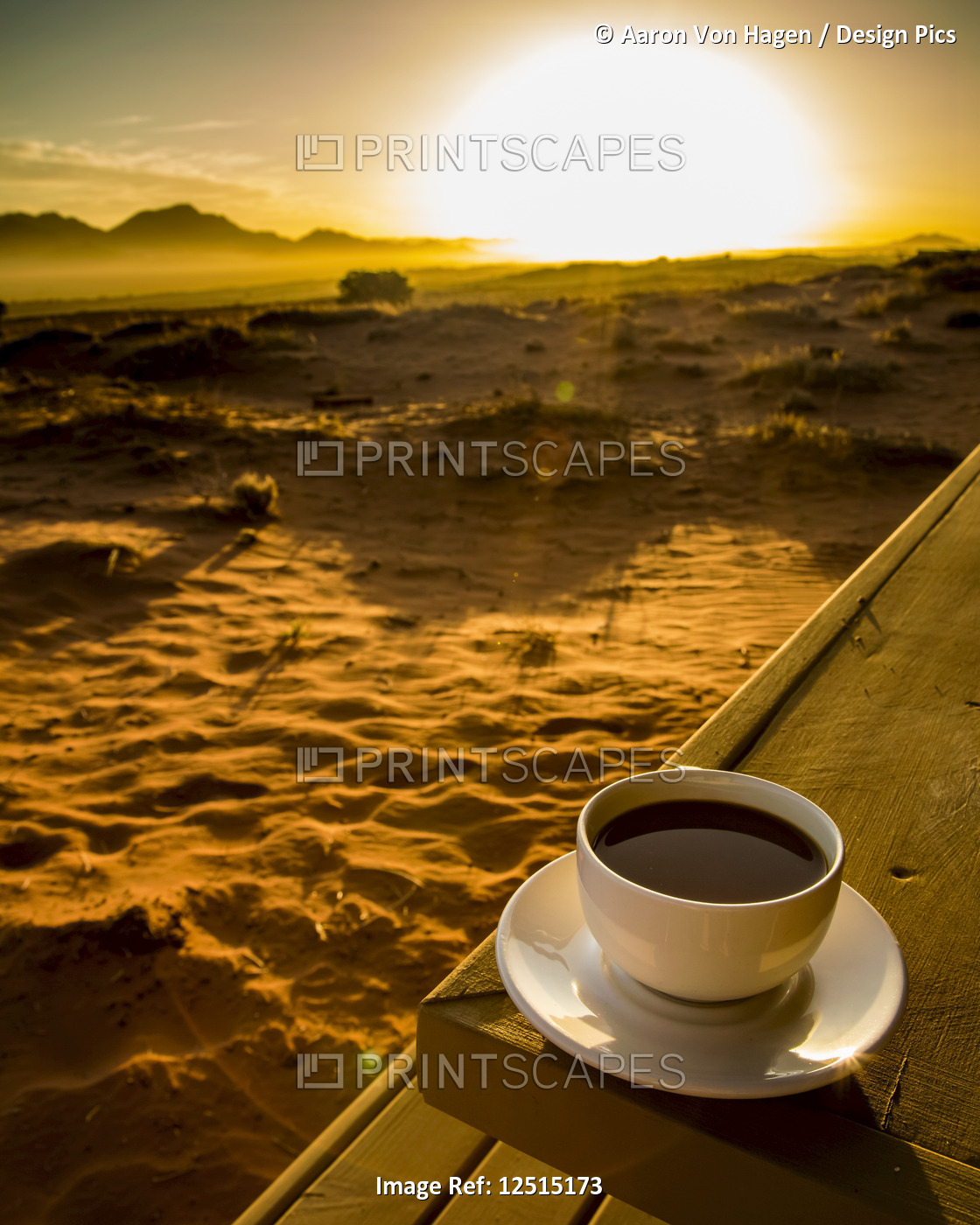 A cup of coffee sits on a wooden table with a view of the sunrise over the ...