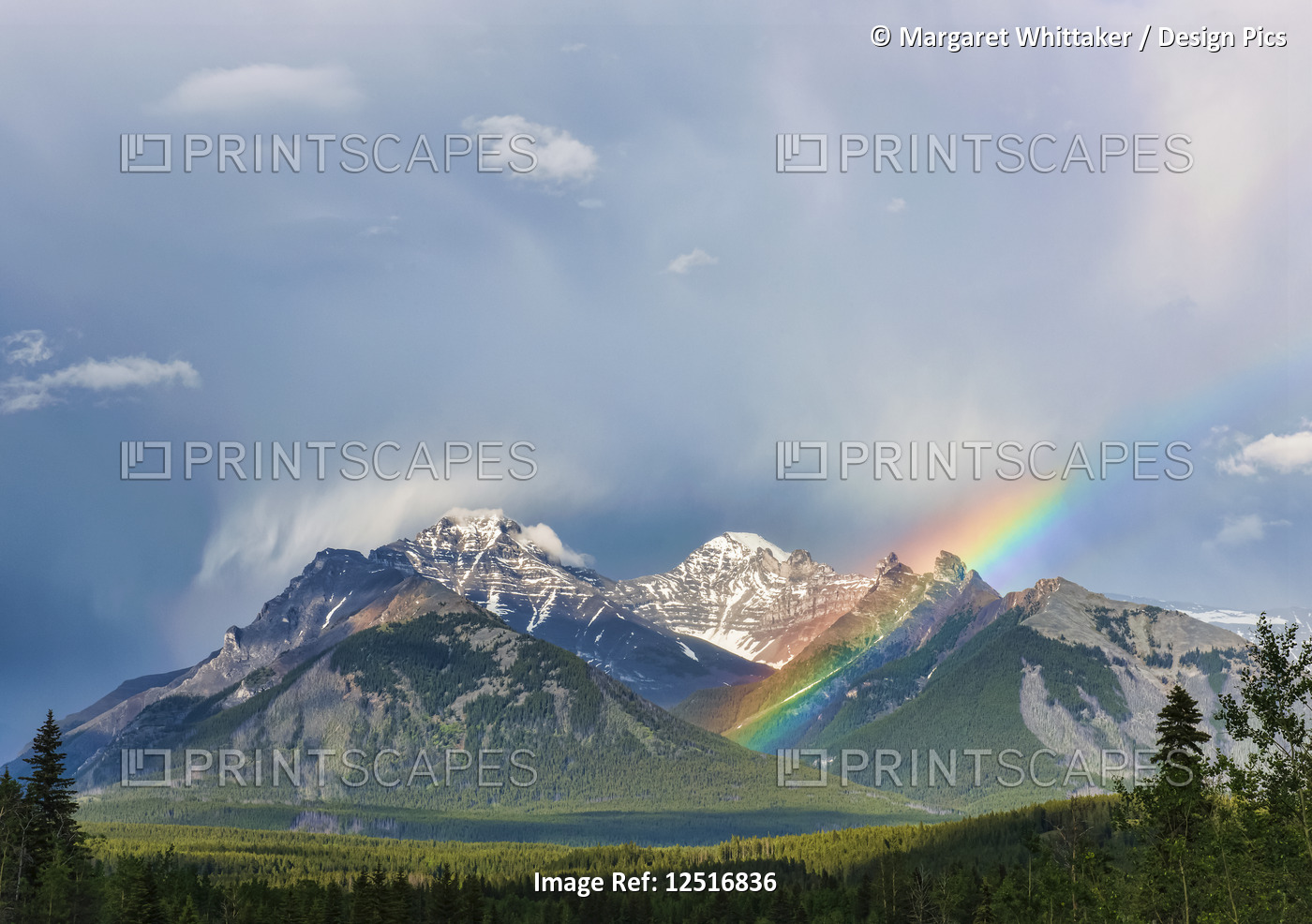 A rainbow emerges between rugged mountain peaks during a heavy rain storm; ...