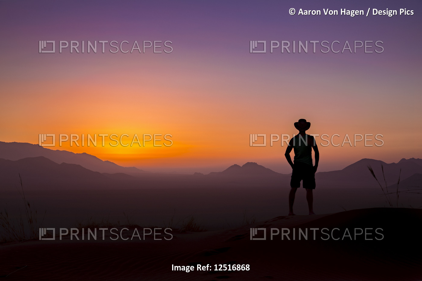Silhouette of a man wearing a cowboy hat stands looking out at the glowing ...