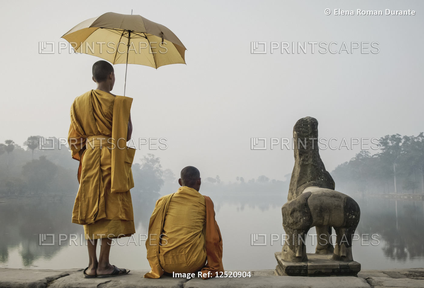 Buddhist monks at the water's edge looking out over a misty river and holding ...