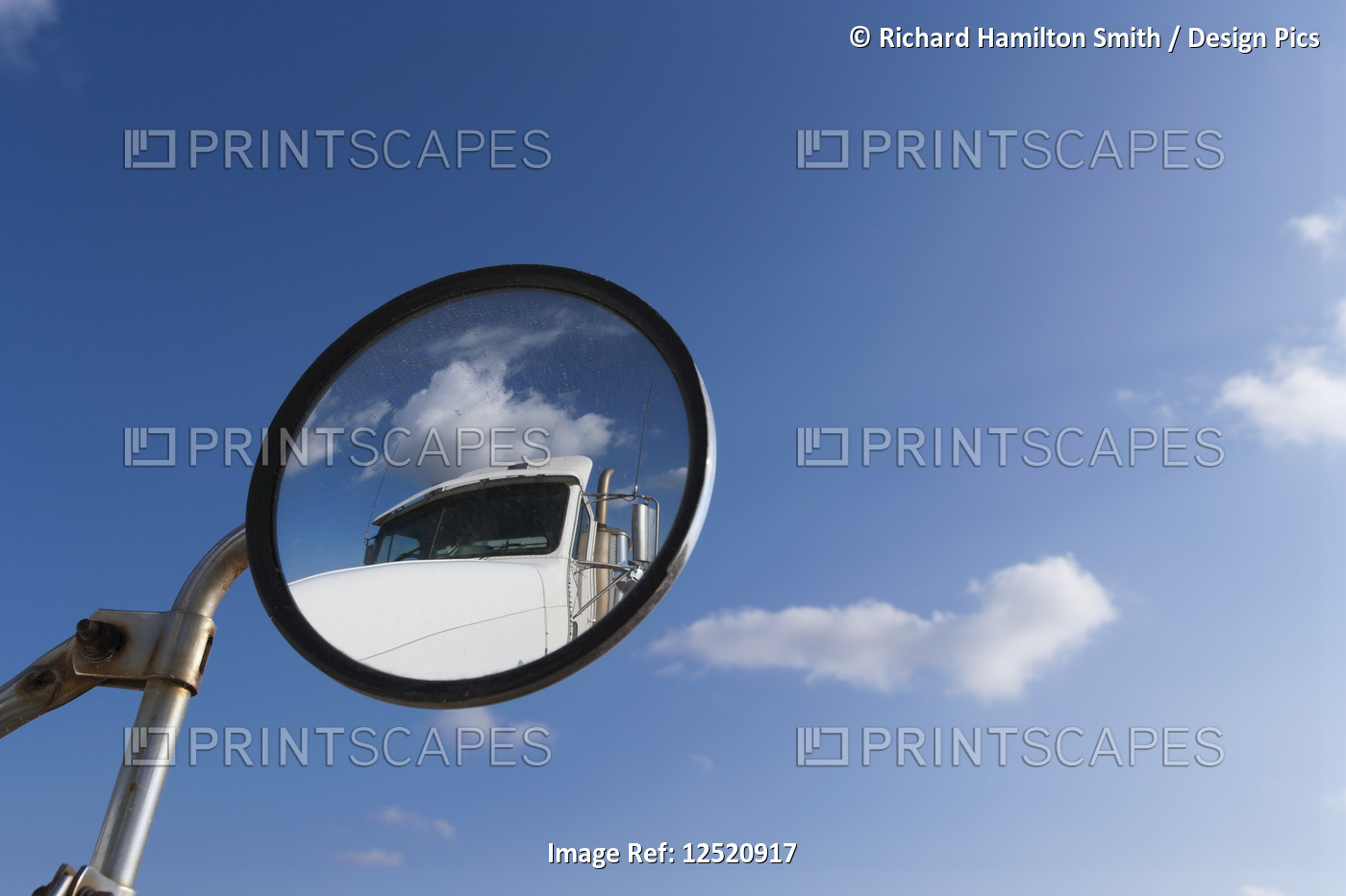 A transport truck reflected in the round side mirror of another truck with blue ...