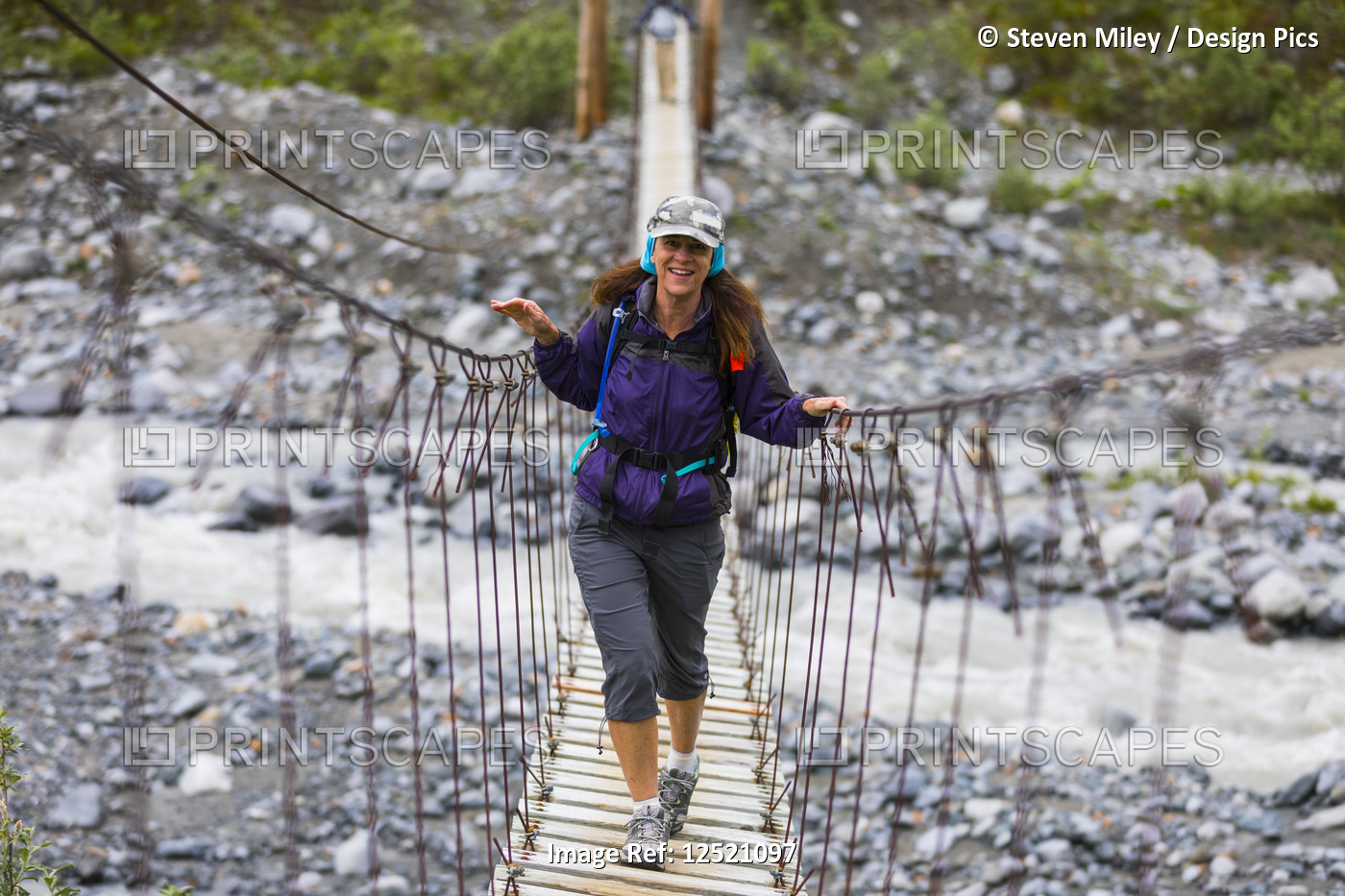 Female hiker crosses a wooden foot bridge on her way to Gulkana Glacier; ...