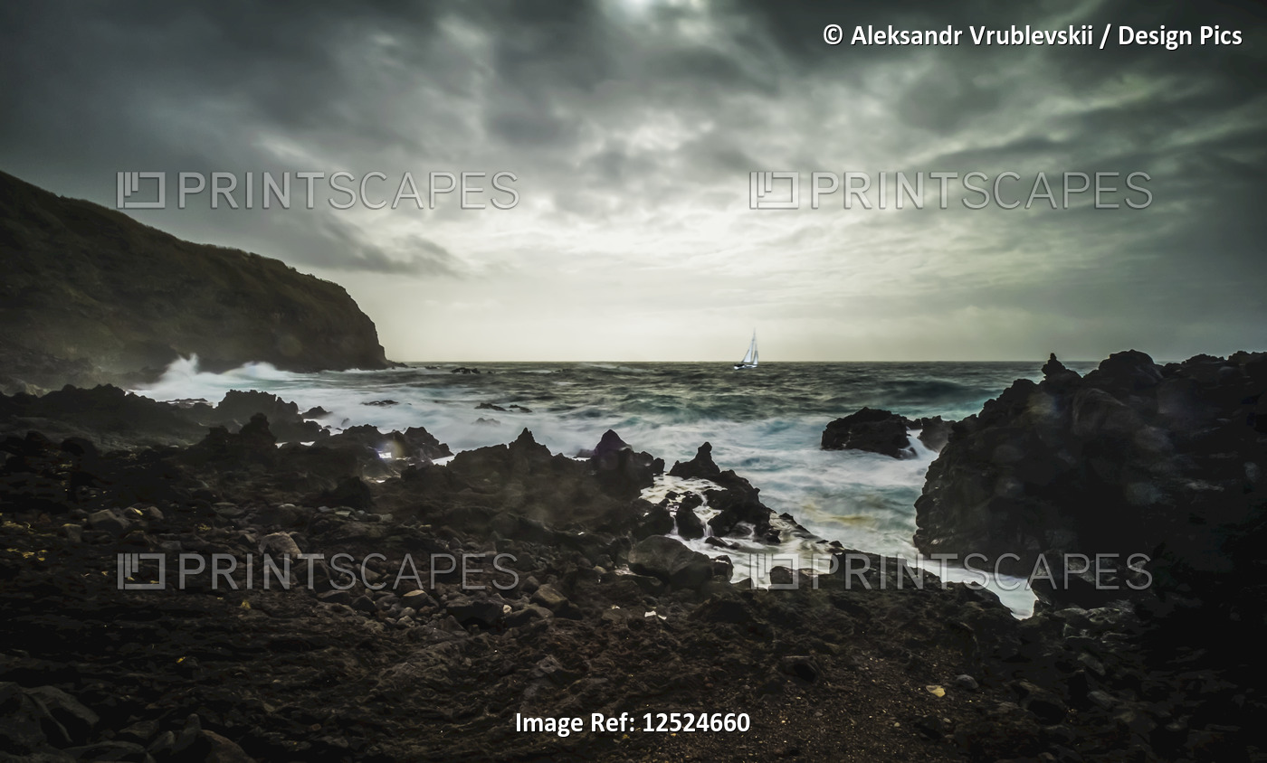 Rugged landscape along the Atlantic coast with a yacht in a storm; Sao Miguel ...
