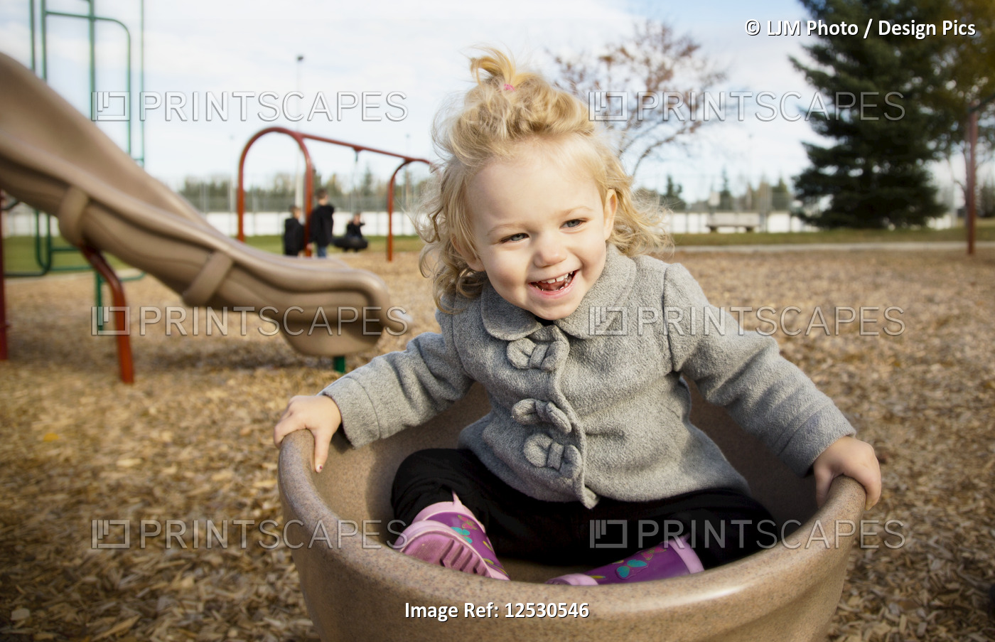 A cute young girl spinning in a saucer on a playground during the fall season; ...