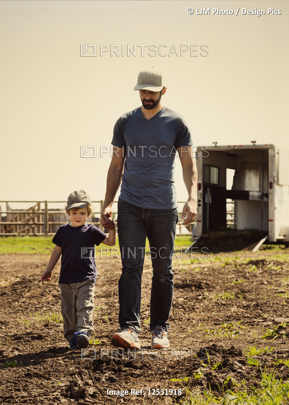 A father walks and holds hands with his young son on a farm; Edmonton, Alberta, ...