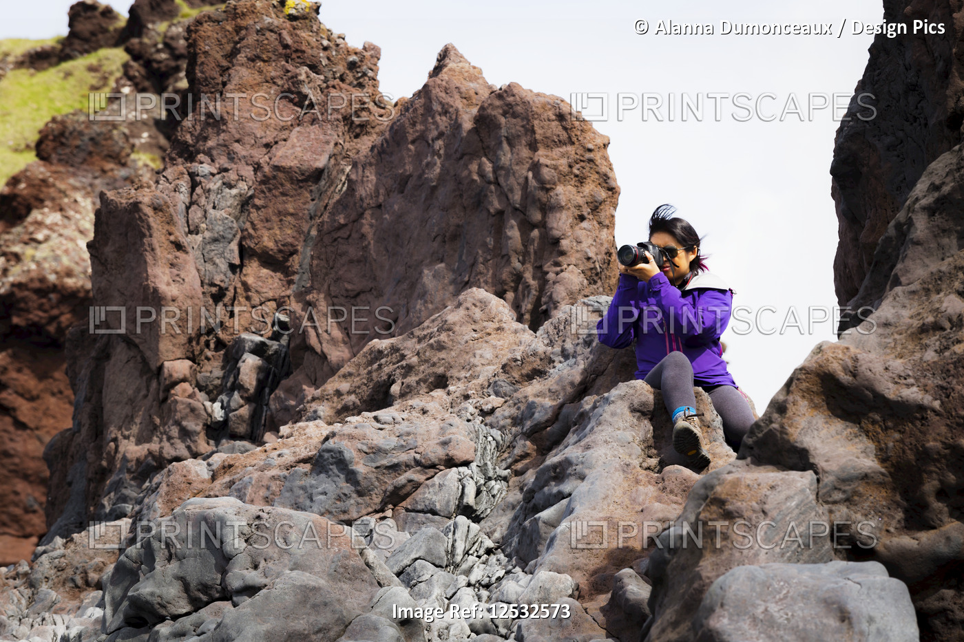 A tourist sits on the top of a rock formation to take a higher photo of the ...