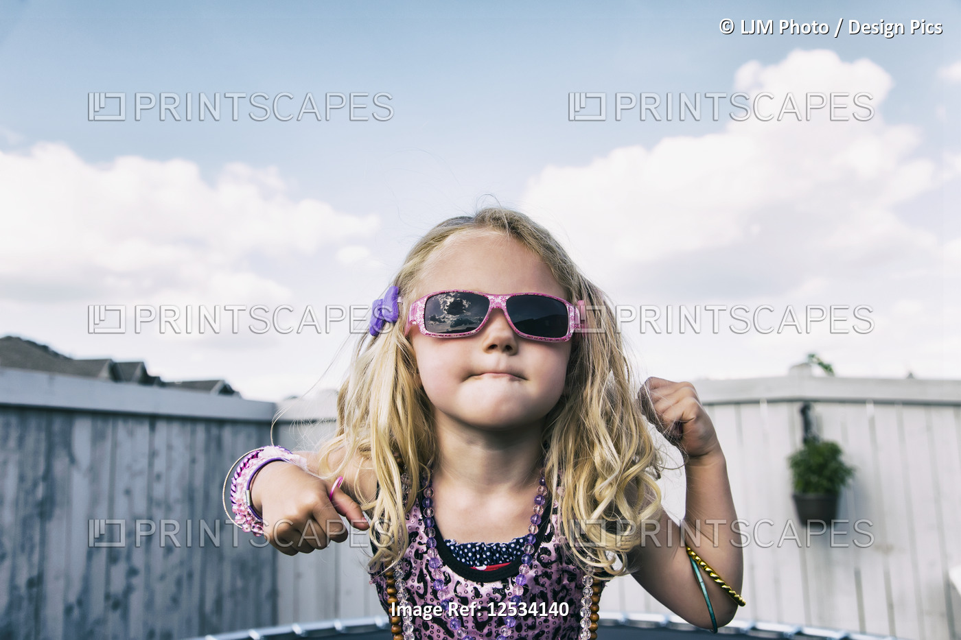 A young girl all dressed up with blond curly hair, sunglasses and jewelry ...