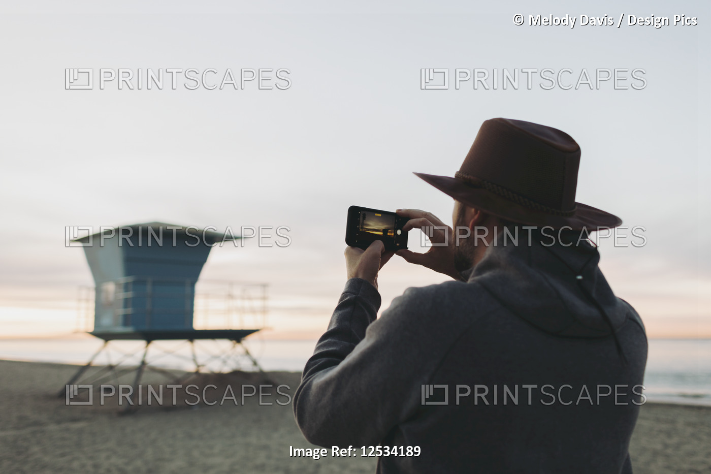 A man stands photographing a lifeguard station at dusk; Long Beach, California, ...