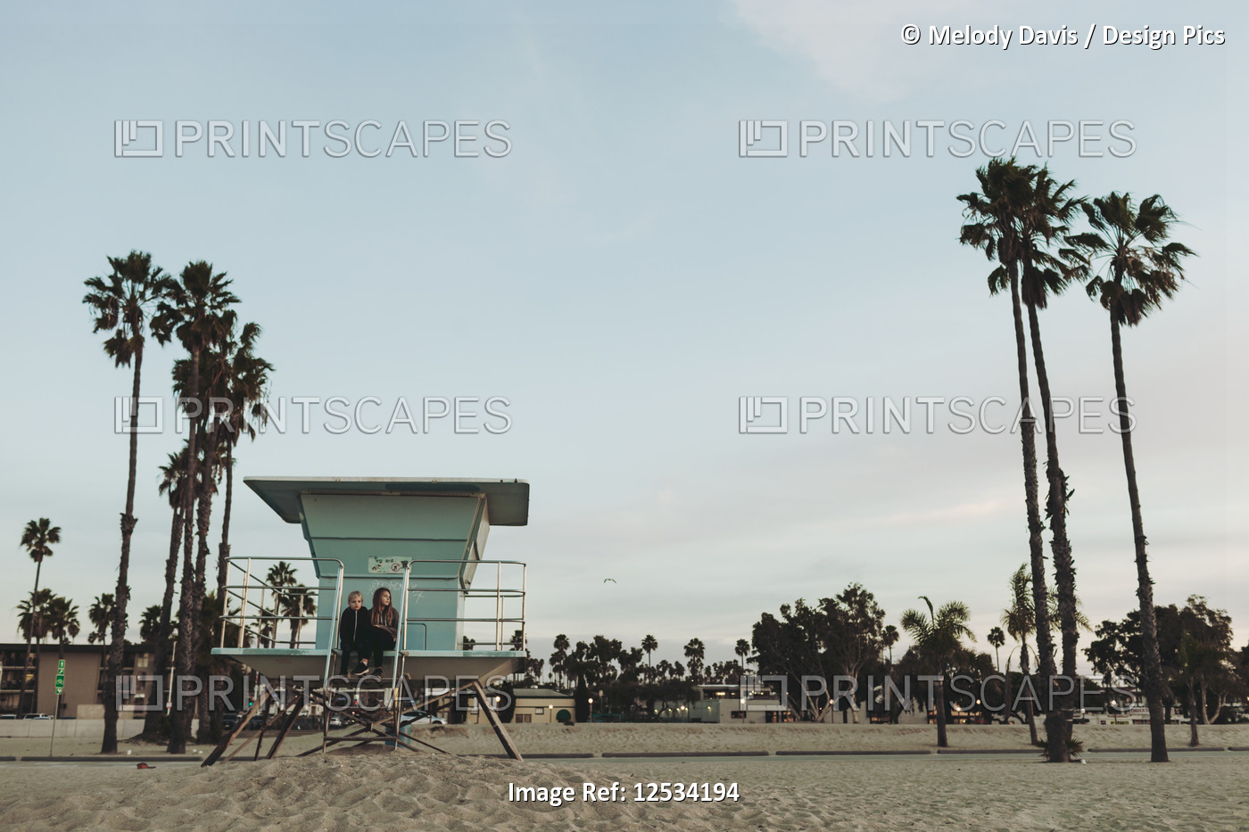 Two girls sit on a lifeguard station at dawn looking out to the ocean; Long ...