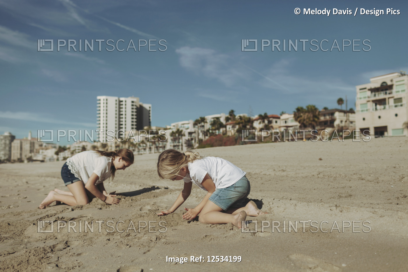 Two girls playing in the sand at the beach with condominium buildings in the ...