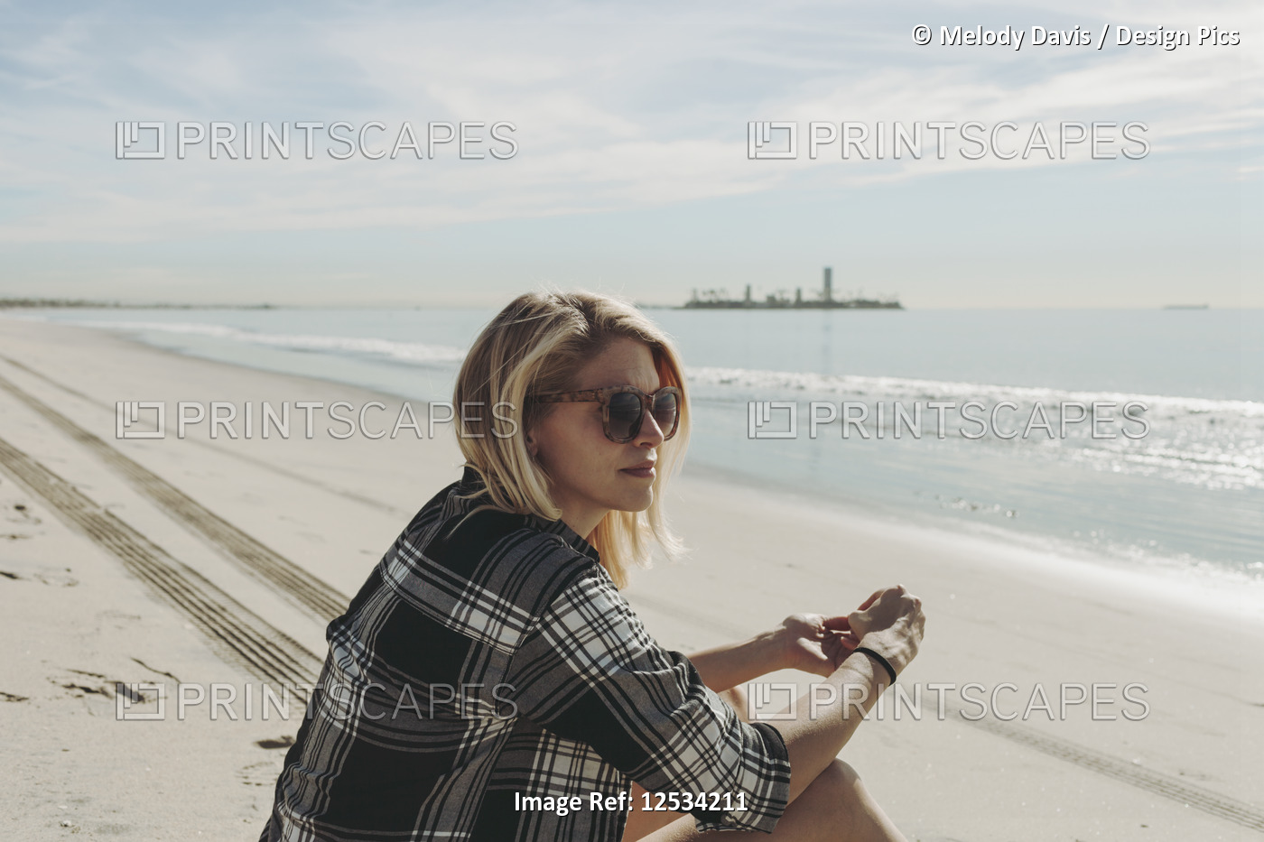 A woman sits on a beach looking out to the water; Long Beach, California, ...