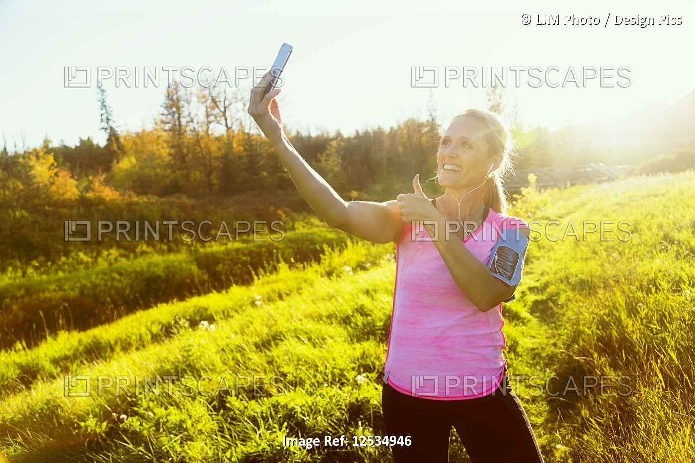 An attractive middle-aged woman wearing active wear pauses to take a selfy with ...