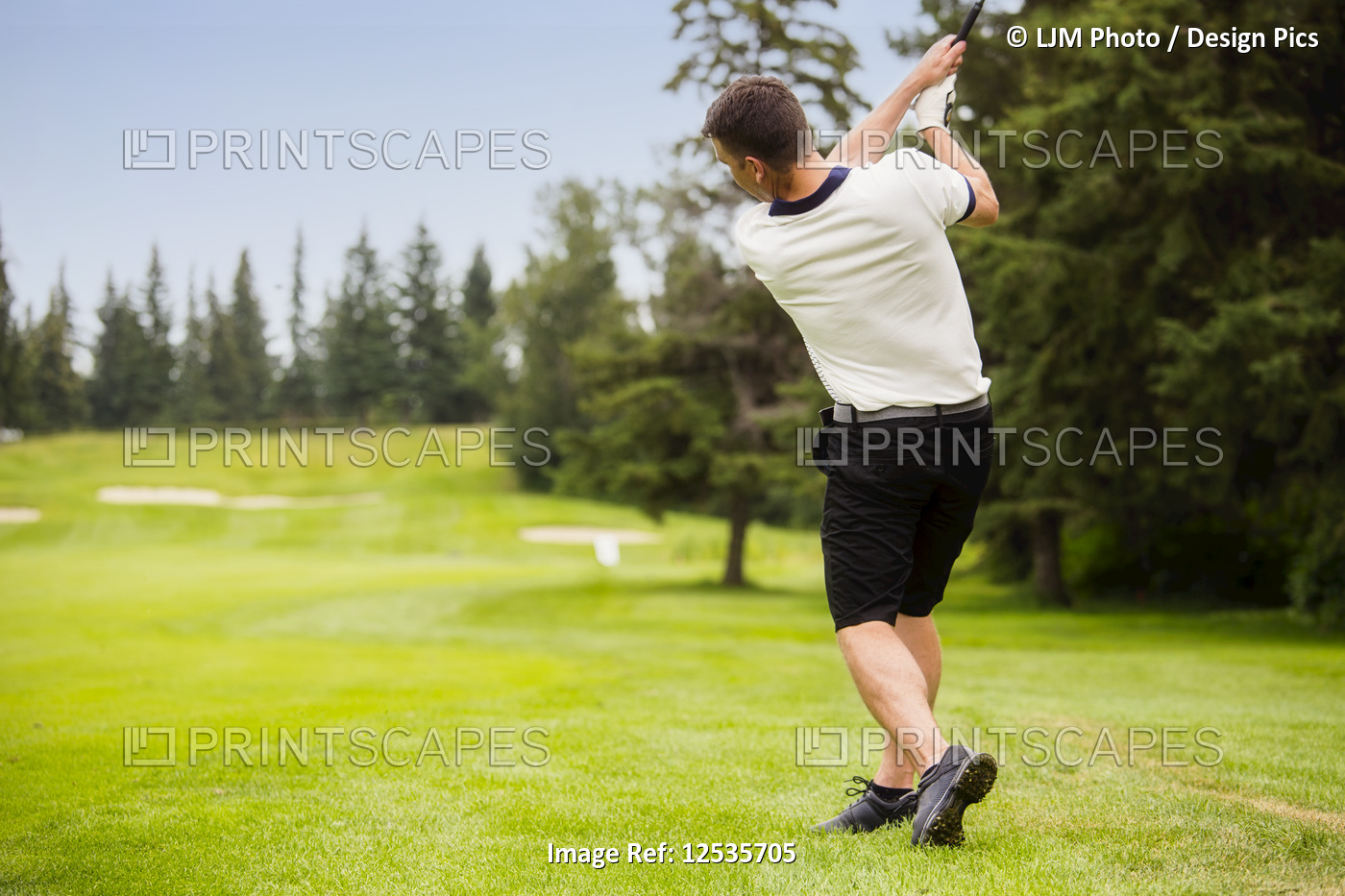 A male golfer driving a golf ball down the fairway of a golf course with the ...