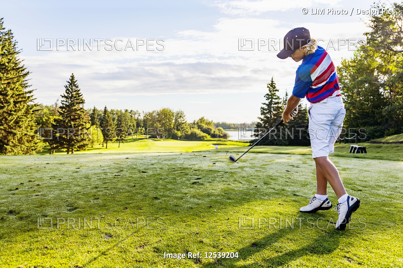 A young male golfer drives a ball down a fairway at a golf course during a ...