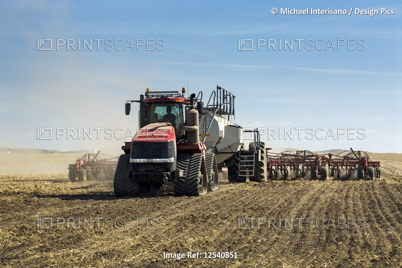 Tractor pulling an air seeder, seeding a field with blue sky and clouds in the ...
