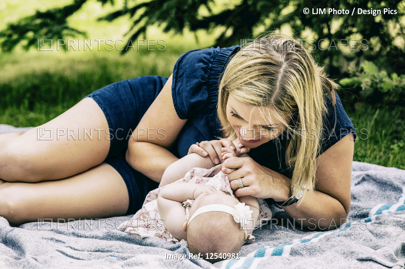 A young mother playing with her baby on a blanket in a city park on a warm ...
