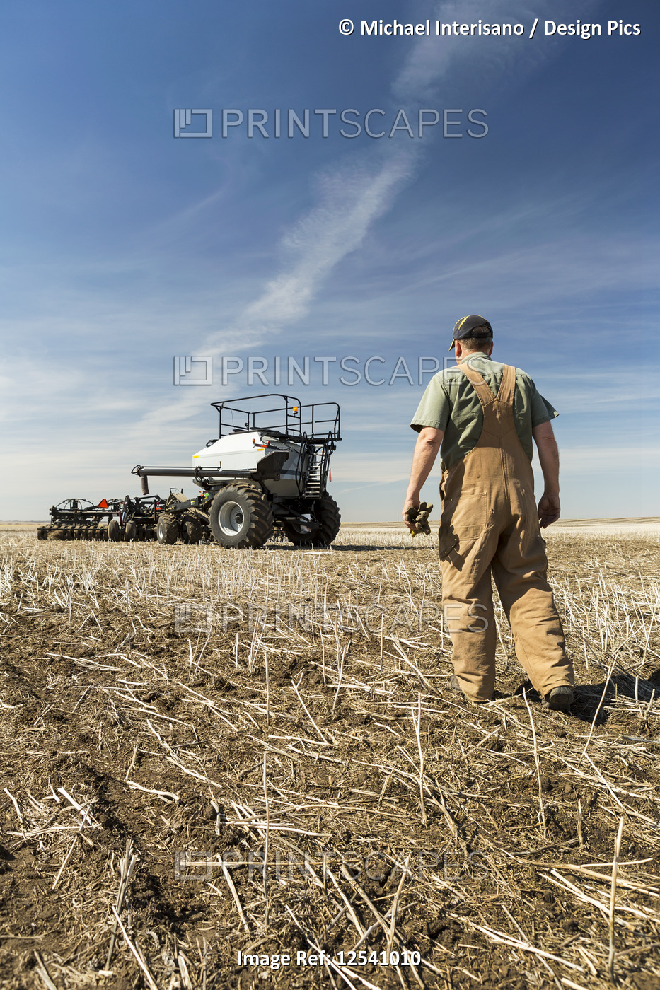 Farmer walking towards hopper and air seeder in a canola stubble field with ...
