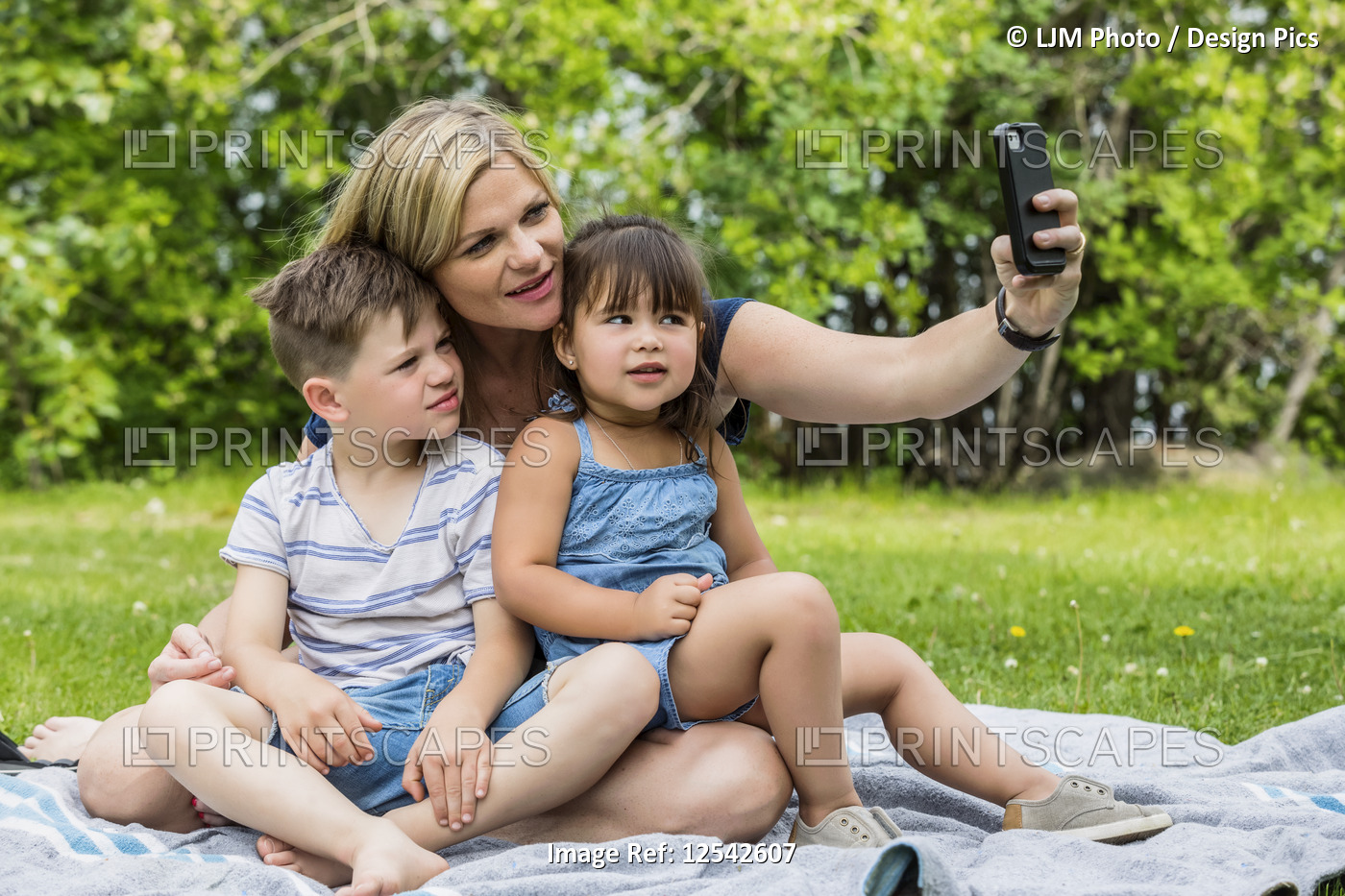 A young mother taking a self-portrait with her son and daughter in a park; ...