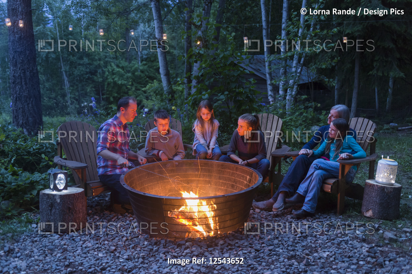 A family gathers outside around a campfire at dusk; Salmon Arm, British ...