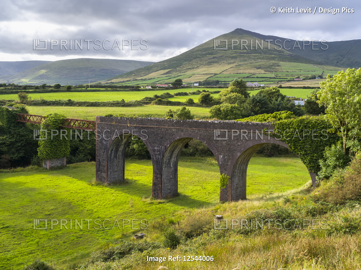 Bridge crossing over lush countryside with bright green fields and mountains in ...