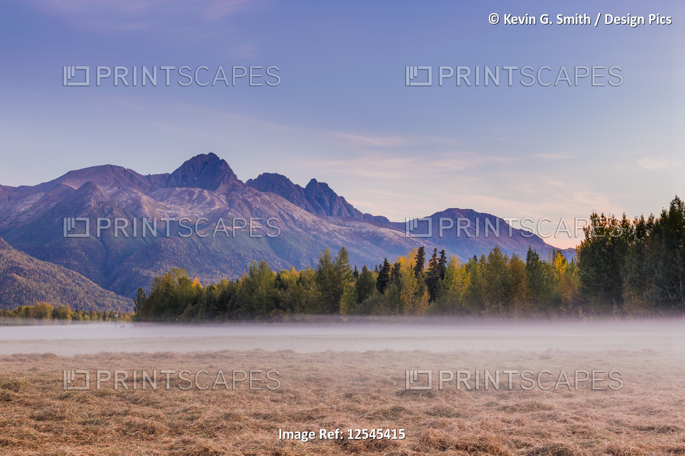 Fog fills a grassy field below Twin Peaks and the Chugach Mountains during ...