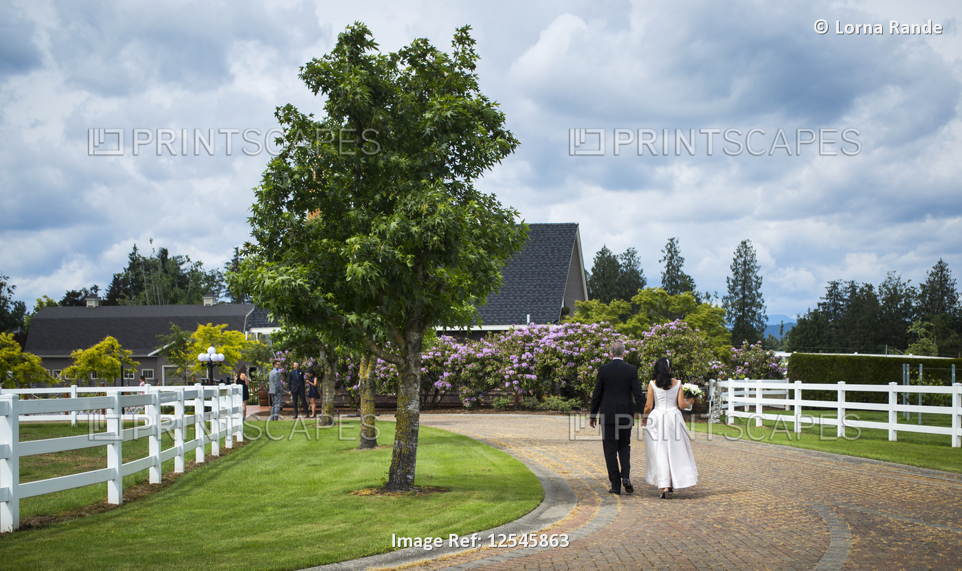 Bride and groom walk down a path holding hands; Langley, British Columbia, ...