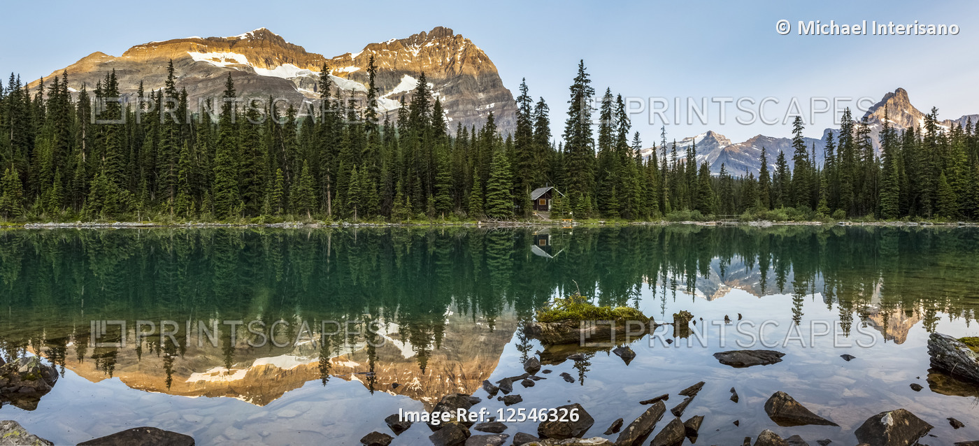 Panorama of mountain range reflecting in an alpine lake with the glow of warm ...