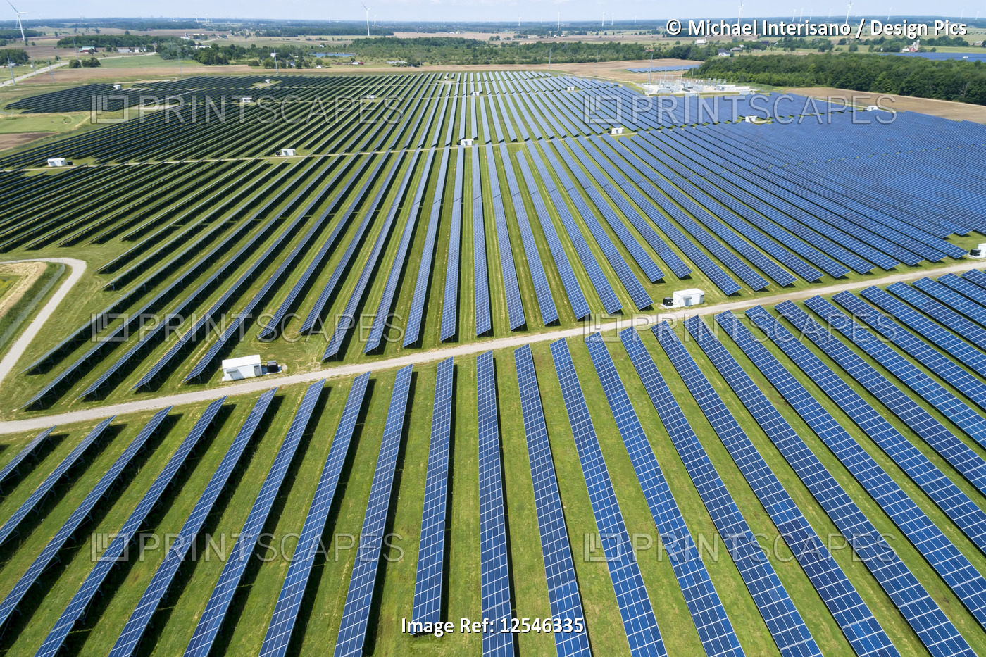 Aerial view of large solar farm with panels reflecting sunlight and windmills ...
