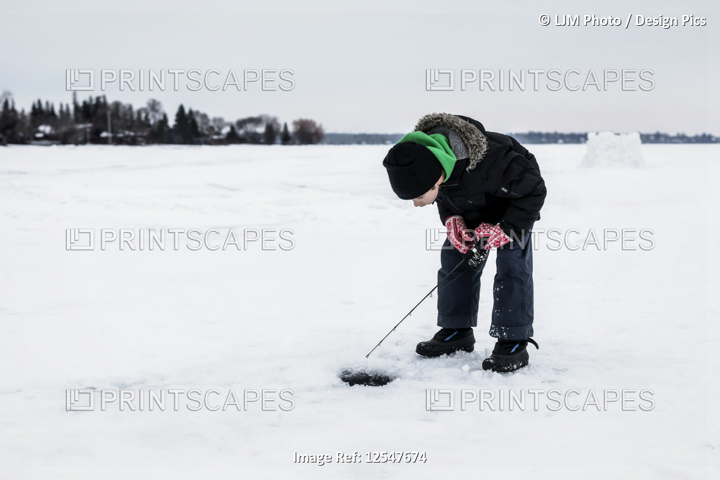 Boy patiently waiting for a bite while ice fishing and looking down the hole on ...