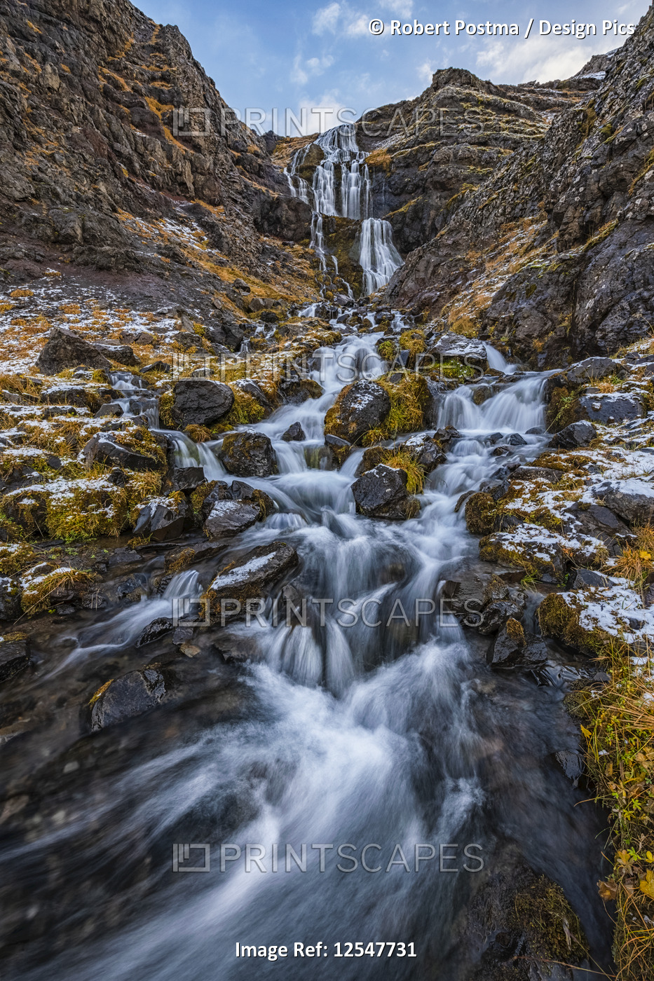 Waterfall along rugged rocks with lichen and moss along the road; Iceland