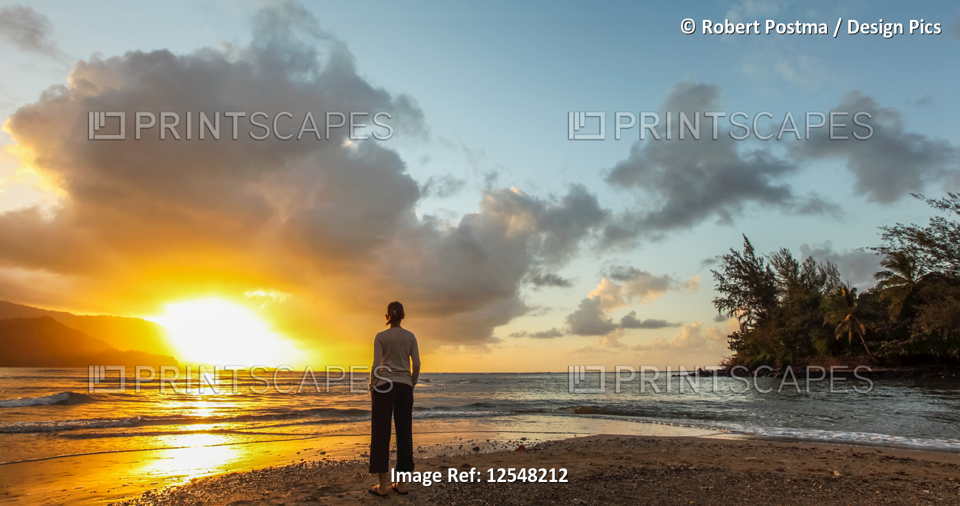 Woman standing on the beach at sunset; Kauai, Hawaii, United States of America