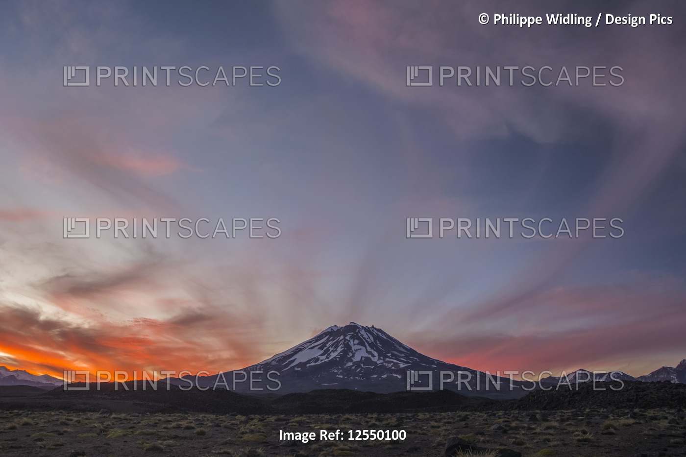 The snow-covered slopes of a volcano are set against a red sunset sky; Mendoza, ...