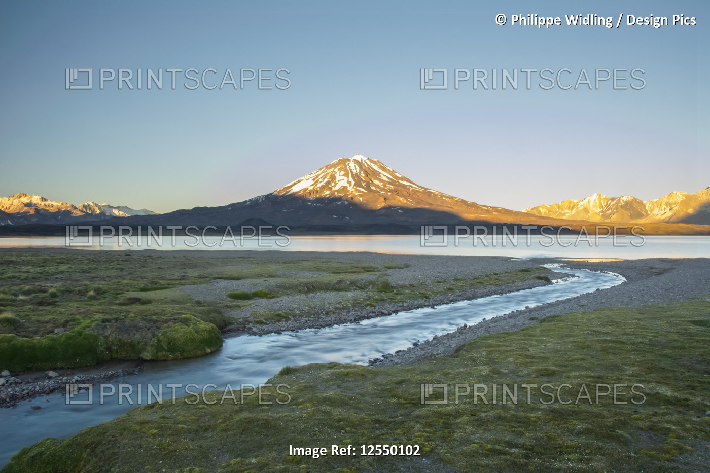 A stream leads the eye towards a high altitude lake. A volcano and snow-capped ...