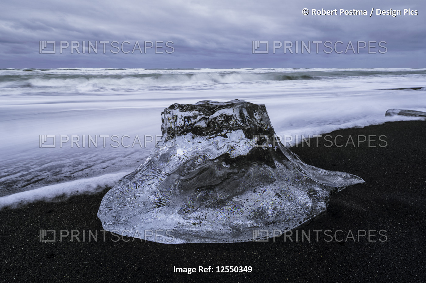 Large chunk of ice sitting on the shore of Iceland with dramatic skies in ...
