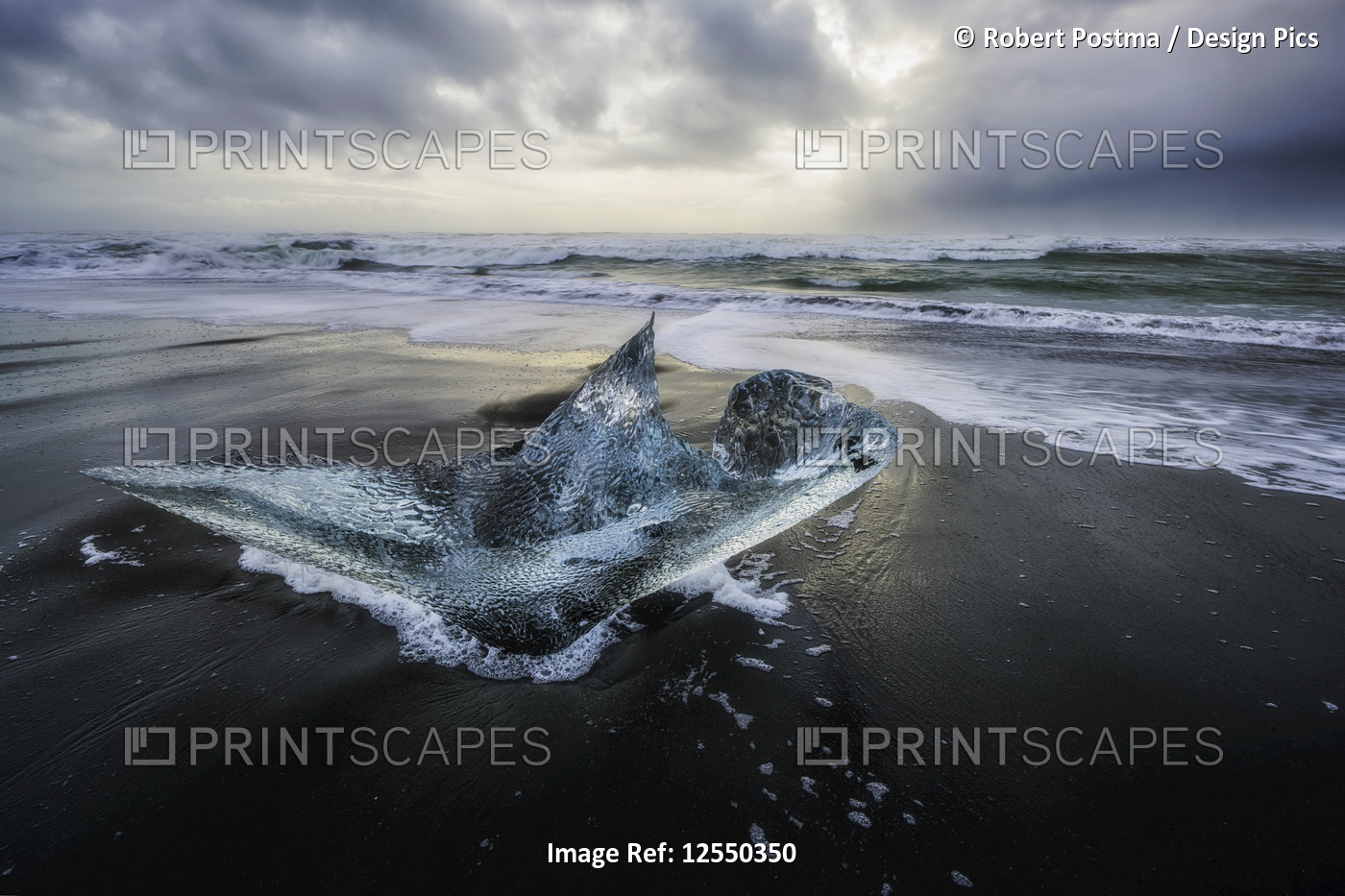 Piece of ice sitting on the shore of Iceland with dramatic stormy skies in ...
