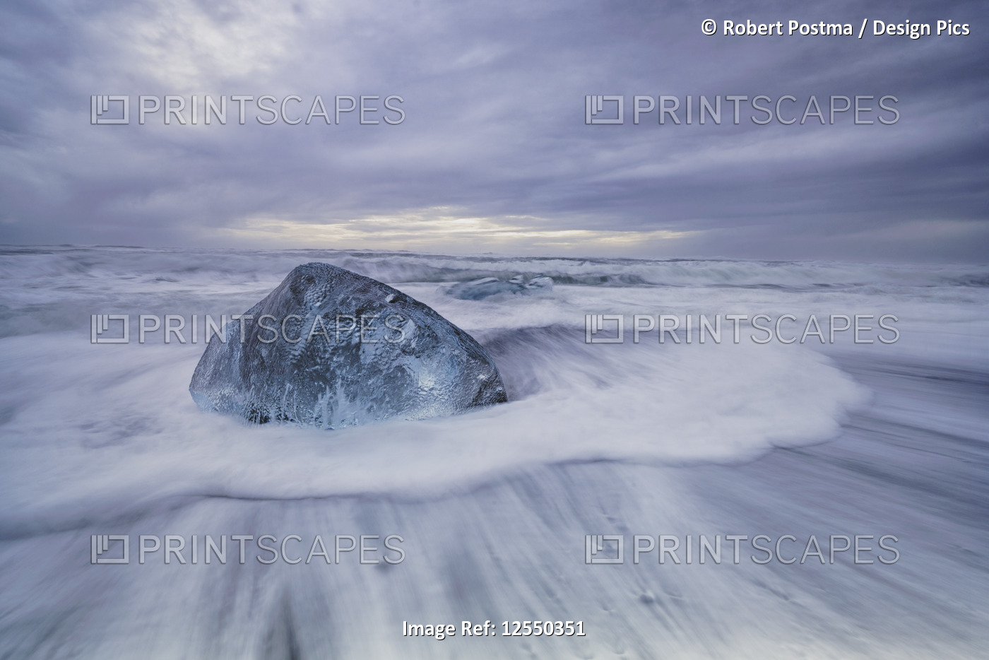 Large ice block laying on the shores of Southern Iceland while waves crash on ...