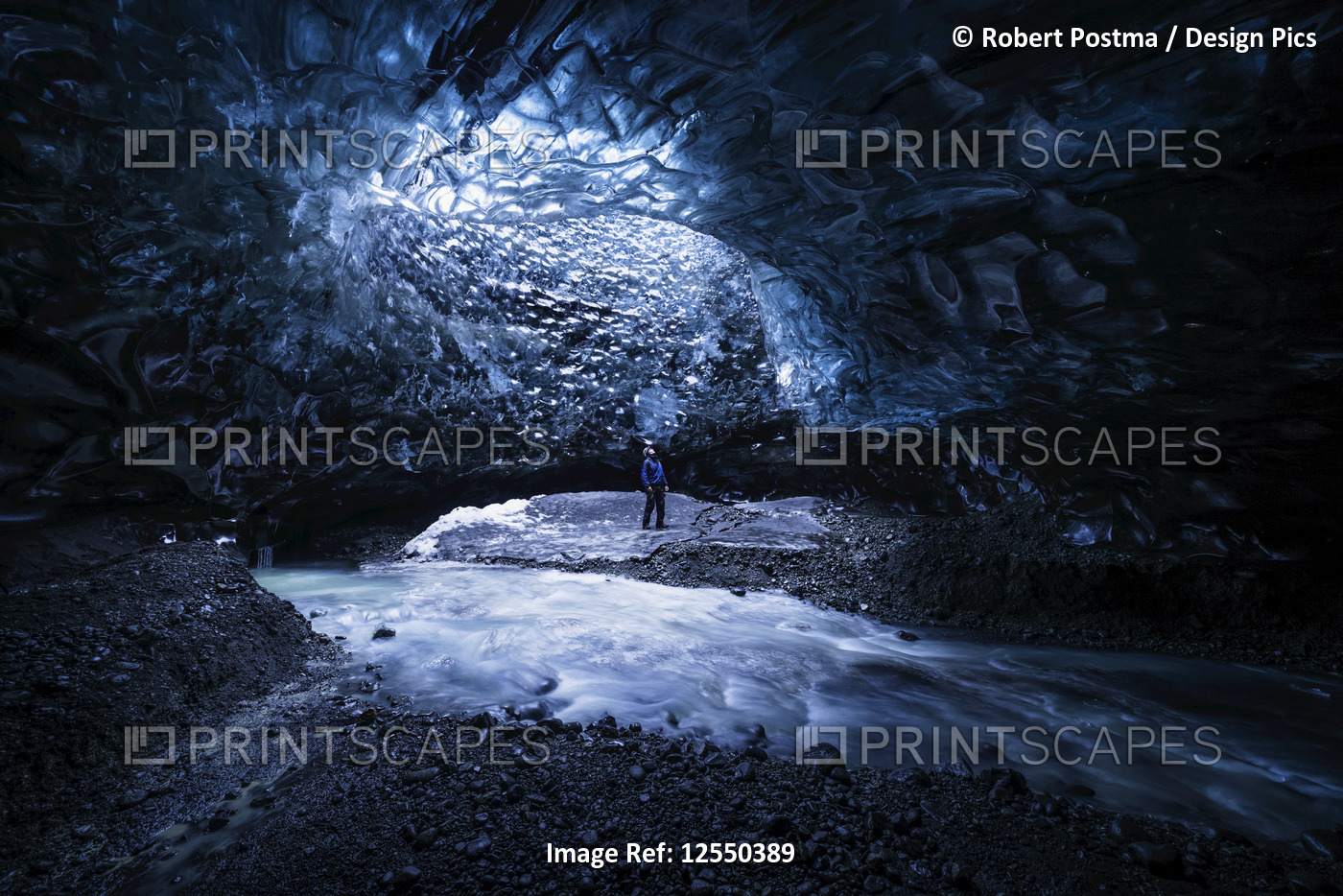 Man standing under an opening in the ice cave while walking beneath a glacier: ...