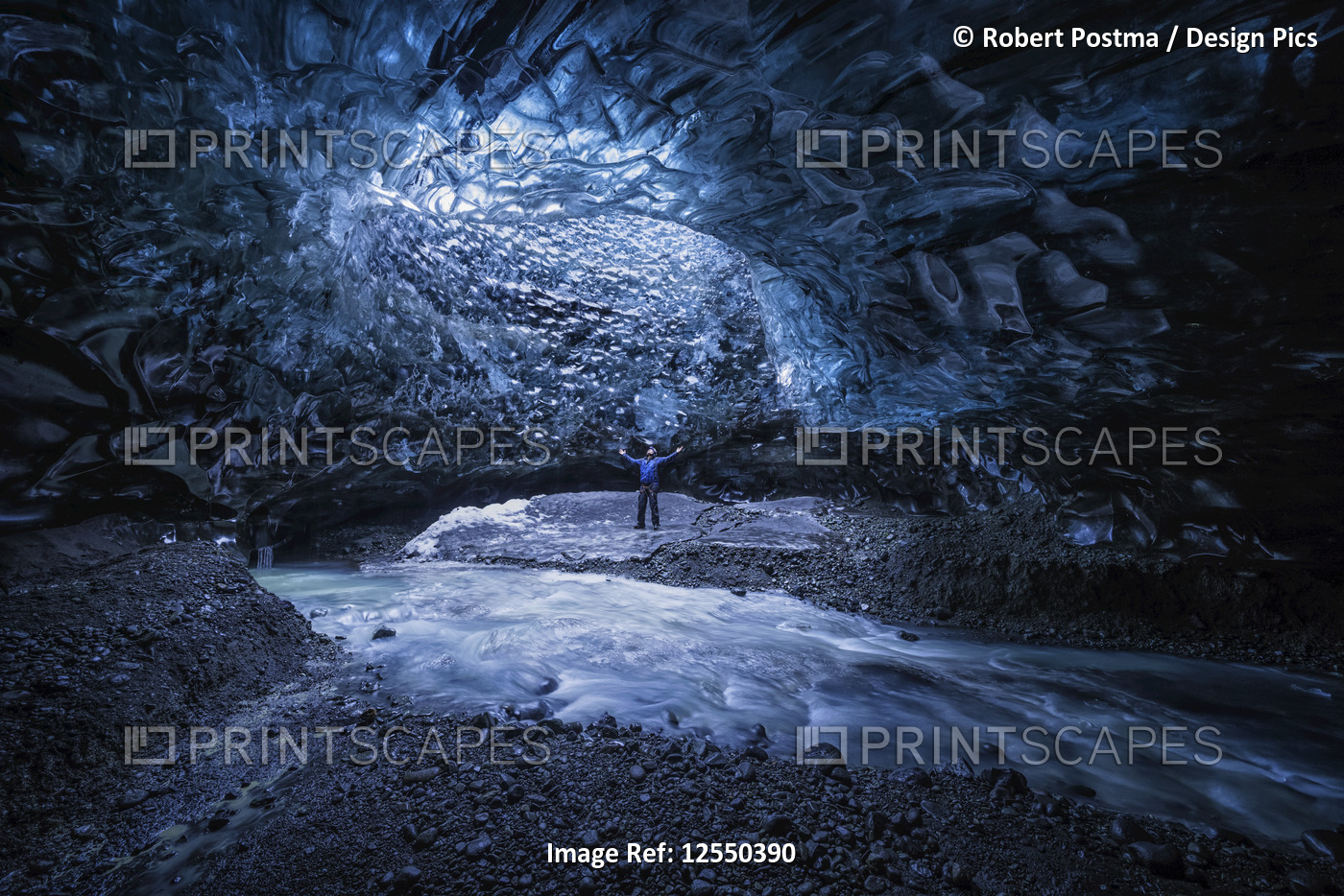 Man standing under an opening in the ice cave while walking beneath a glacier: ...