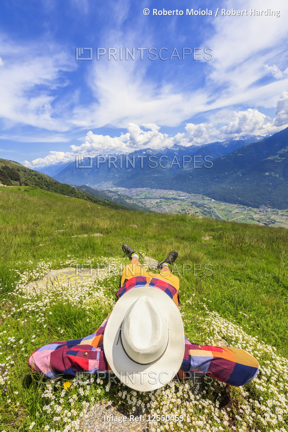 Rear view of man with hat lying on grass, Alpe Bassetta, Valtellina, Sondrio, Lombardy, Italy