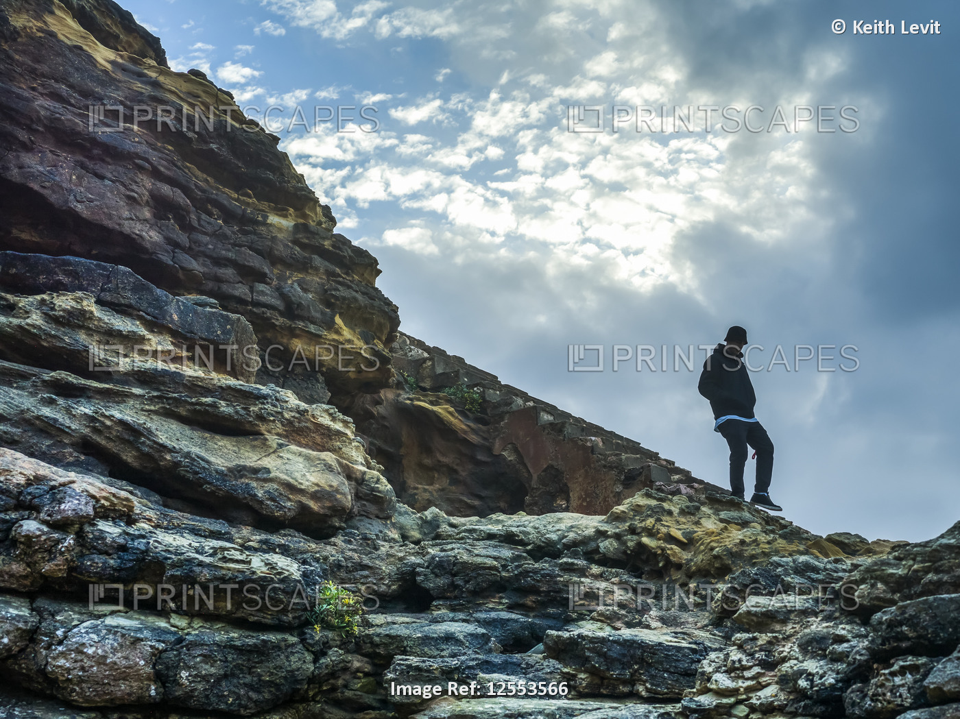 Young man walking on rocky, rugged terrain along Nazare Beach; Nazare, Leiria ...
