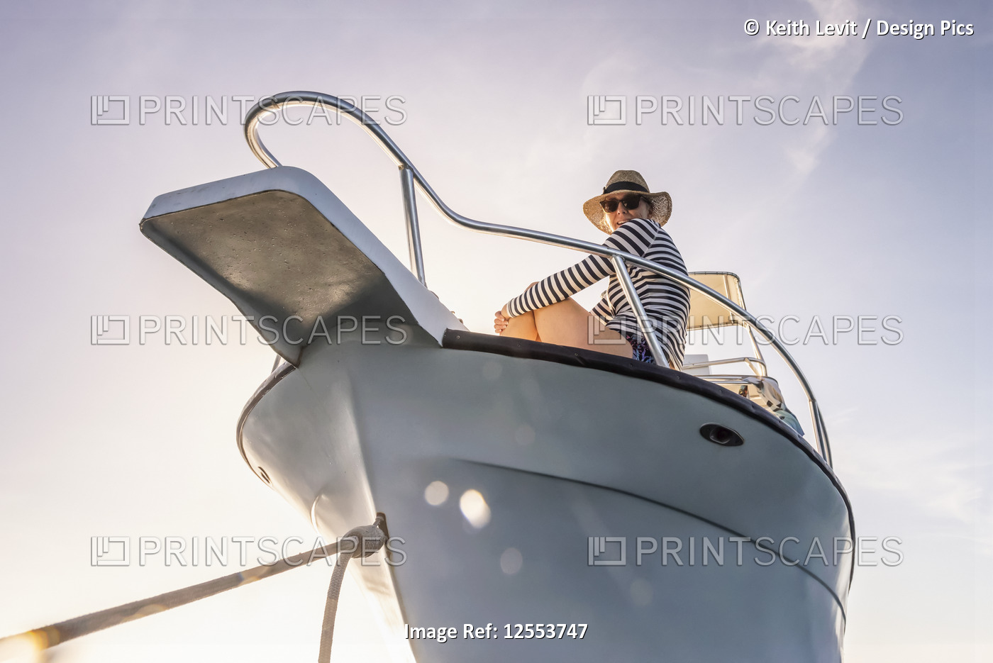 A woman wearing sunglasses and a sun hat looks down at the camera from the deck ...