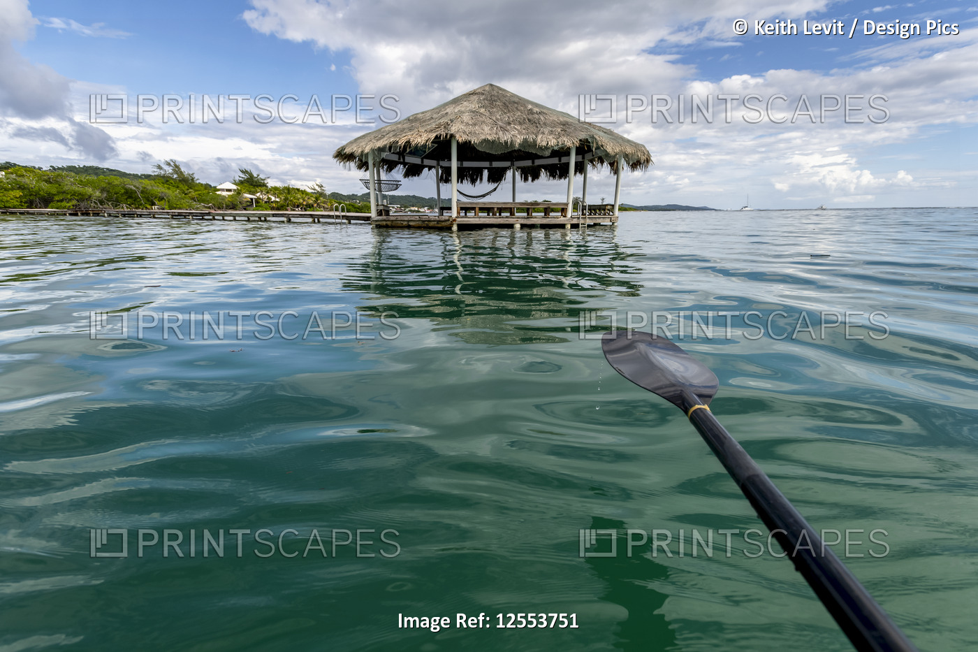 A boat paddle over turquoise water with a shelter at the end of the dock and ...