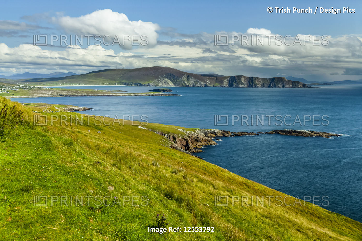 Bright blue water and lush green grass along the coastline of Achill Island on ...