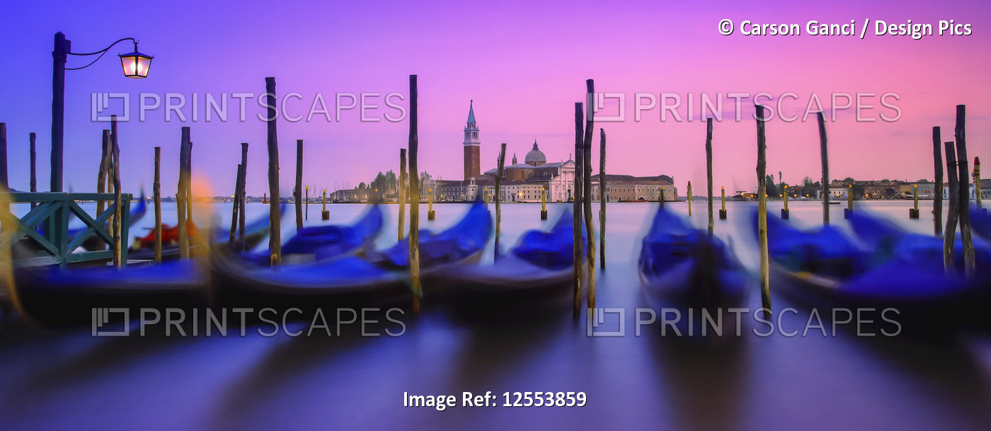 Gondolas moored along the shoreline of the Grand Canal during a vibrant sunset ...
