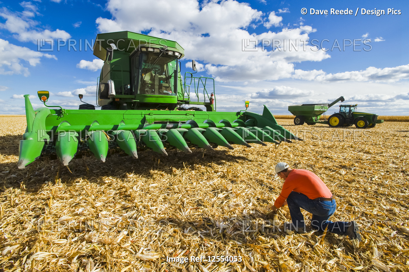 A farmer examines corn residue in front of a combine harvester  with a tractor ...