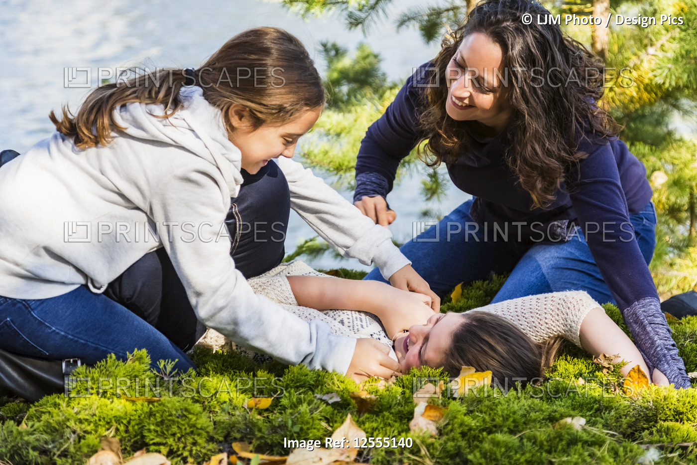 A mom and her two daughters fooling around and tickling each other beside a ...