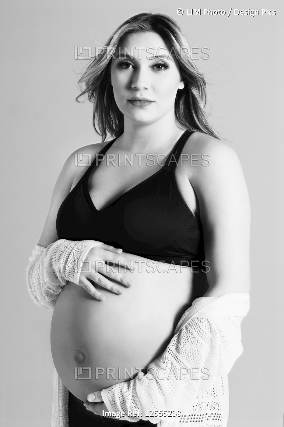 A black and white photo of a young pregnant woman holding her belly in a studio ...