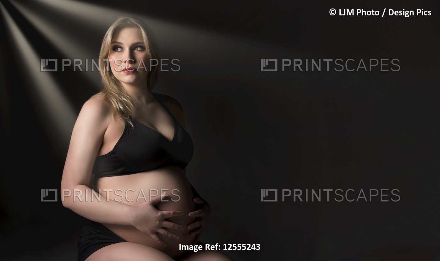 A young pregnant woman holding her belly in a studio and looking away from the ...